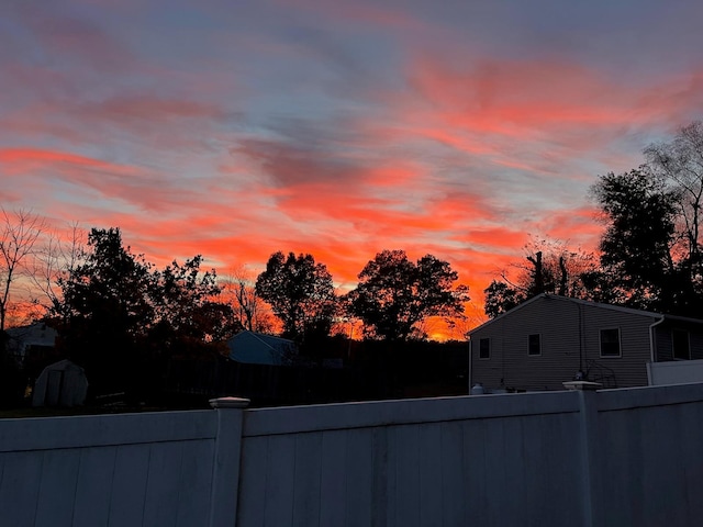 yard at dusk with fence, a storage shed, and an outdoor structure