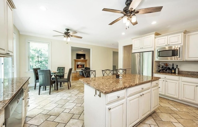 kitchen with appliances with stainless steel finishes, ceiling fan, stone tile floors, a kitchen island, and ornamental molding