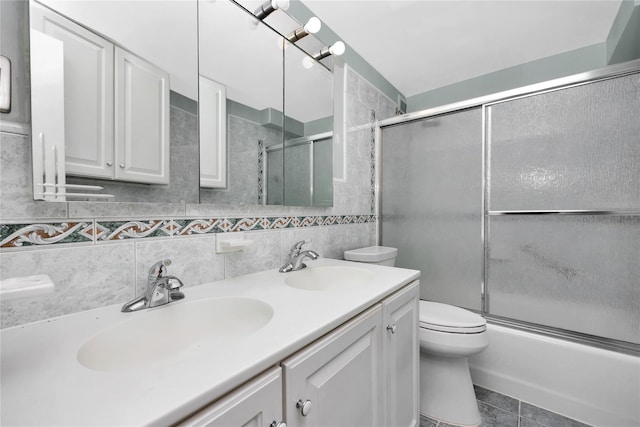 full bath featuring double vanity, tile walls, toilet, combined bath / shower with glass door, and tasteful backsplash