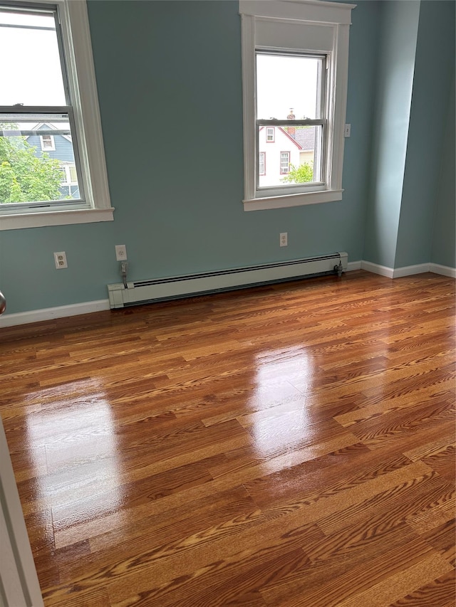 spare room with a baseboard heating unit, wood finished floors, and baseboards