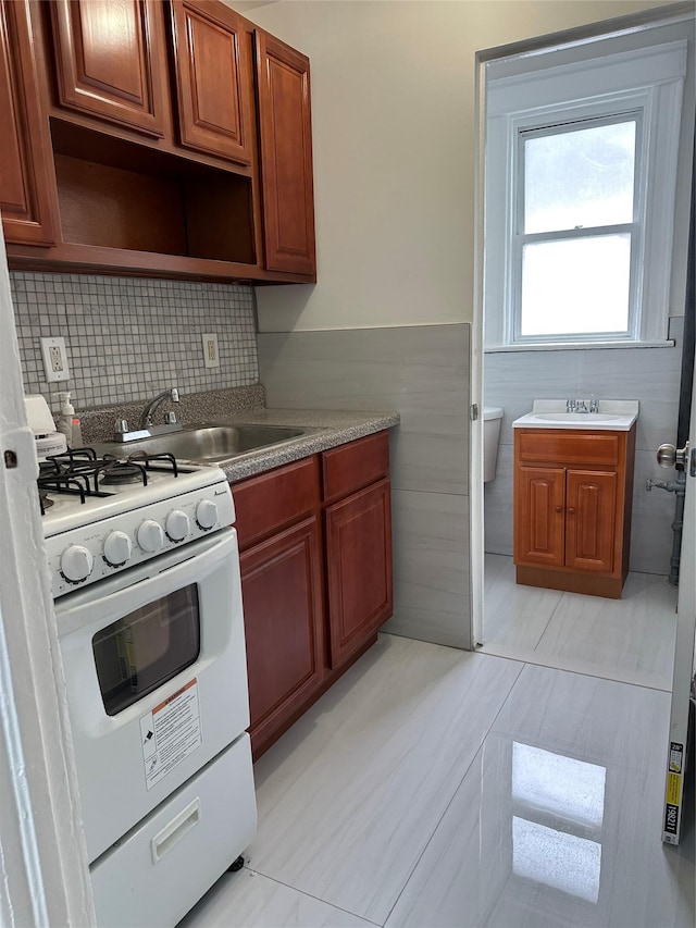 kitchen with white range with gas stovetop, a sink, tile walls, and wainscoting