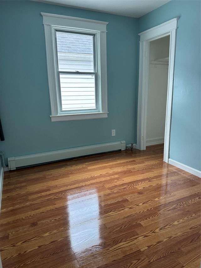 unfurnished bedroom with a baseboard radiator, wood finished floors, a closet, and baseboards
