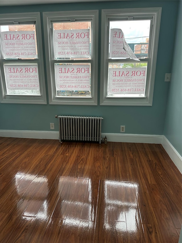 spare room with radiator heating unit, wood finished floors, and baseboards