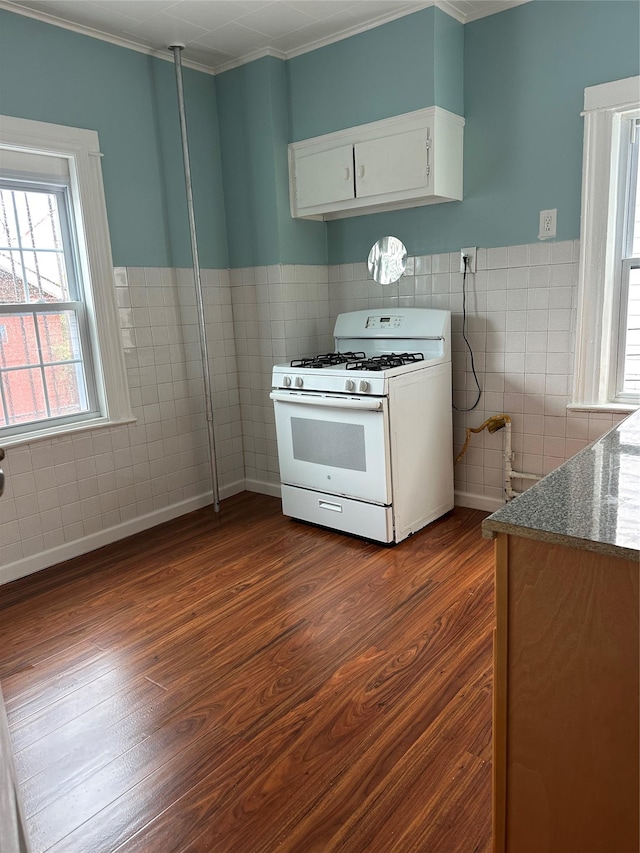 kitchen featuring white range with gas stovetop, tile walls, dark wood-style flooring, crown molding, and white cabinets