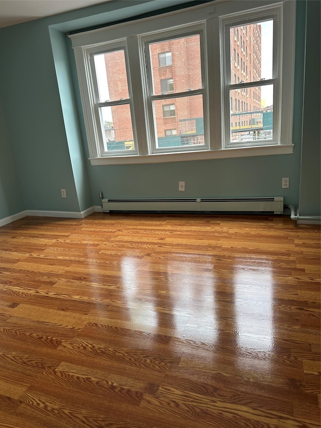 unfurnished room with wood finished floors, a baseboard radiator, and baseboards
