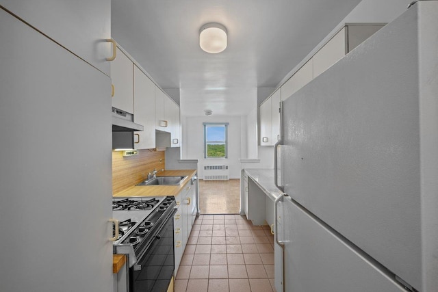 kitchen featuring freestanding refrigerator, black gas stove, radiator, under cabinet range hood, and tasteful backsplash