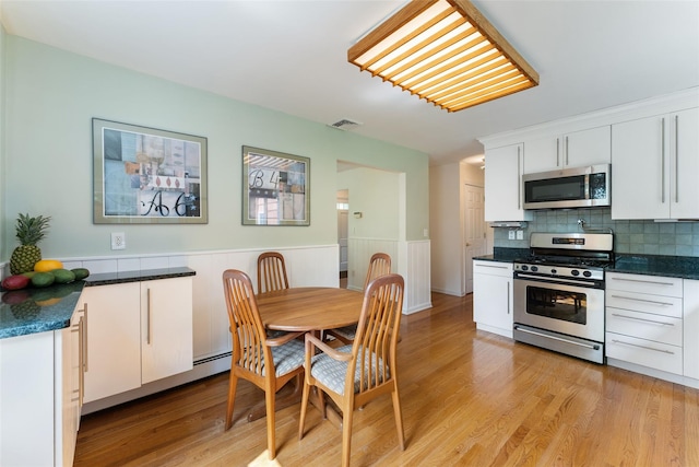 50 Burnside Dr, Hastings-On-Hudson, NY 10706 - kitchen featuring appliances with stainless steel finishes, dark countertops, light wood-type flooring, white cabinetry, and a wainscoted wall