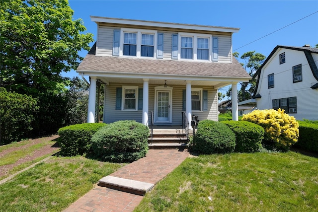 view of front of property with roof with shingles, covered porch, and a front yard