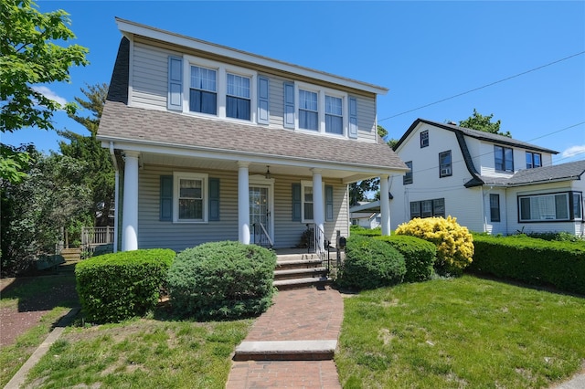 view of front facade with covered porch, a shingled roof, and a front yard