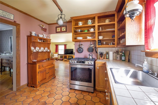 kitchen with tile countertops, gas range, open shelves, a sink, and ornamental molding