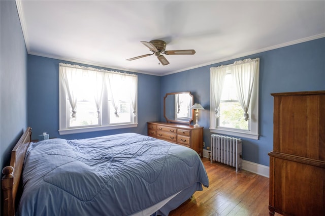 bedroom featuring radiator heating unit, multiple windows, hardwood / wood-style flooring, ceiling fan, and ornamental molding