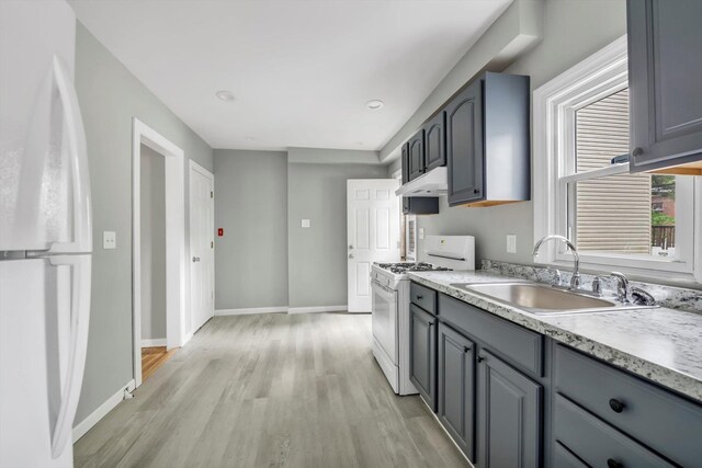kitchen with white appliances, a sink, under cabinet range hood, gray cabinetry, and light wood-style flooring