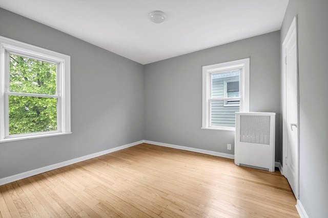 unfurnished room with radiator heating unit, light wood-style flooring, and baseboards
