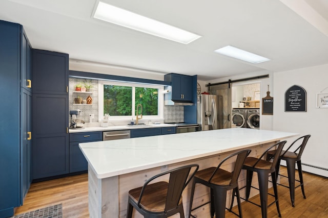 162 Forest Hill Dr, Kingston, NY 12401 - kitchen with appliances with stainless steel finishes, washing machine and clothes dryer, blue cabinets, a breakfast bar area, and light wood finished floors