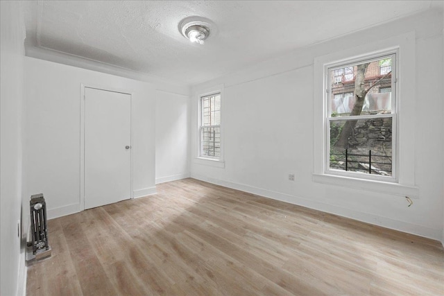 unfurnished bedroom featuring multiple windows, light wood-type flooring, a textured ceiling, and baseboards