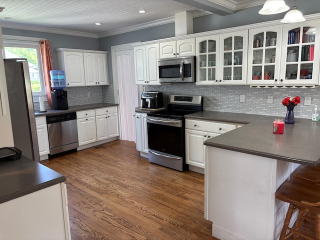 kitchen featuring appliances with stainless steel finishes, a peninsula, dark countertops, a breakfast bar, and white cabinets