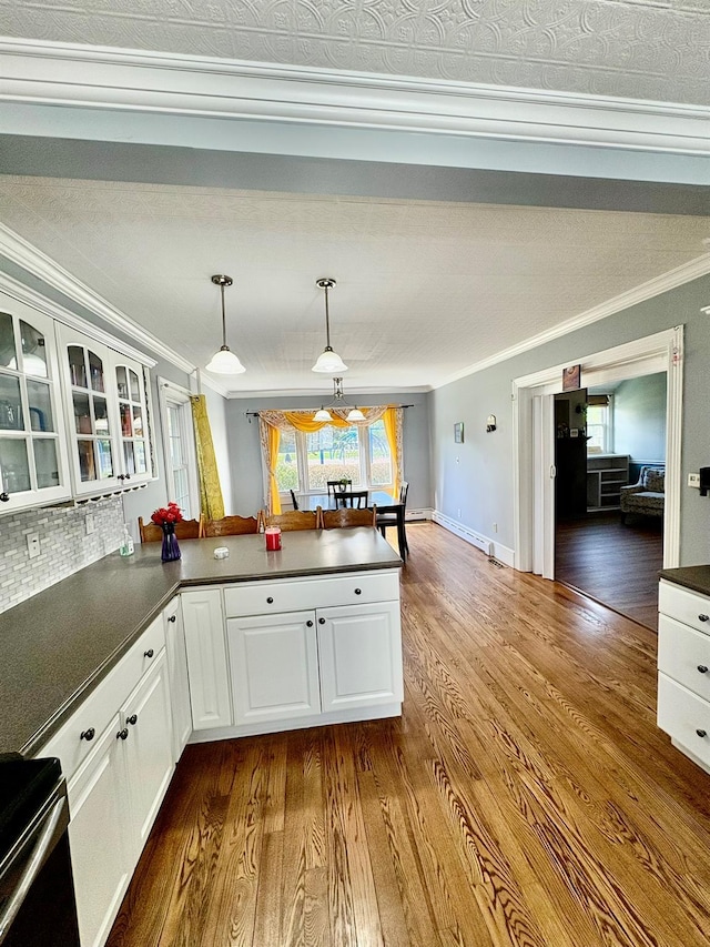 kitchen featuring ornamental molding, dark countertops, a peninsula, dark wood finished floors, and white cabinets