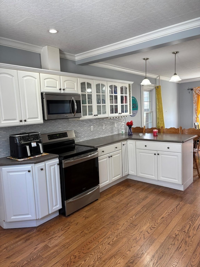kitchen with stainless steel appliances, dark countertops, a peninsula, decorative backsplash, and ornamental molding