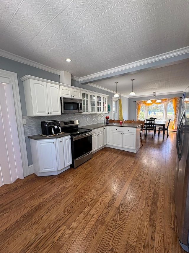 kitchen featuring appliances with stainless steel finishes, a peninsula, dark countertops, dark wood finished floors, and crown molding