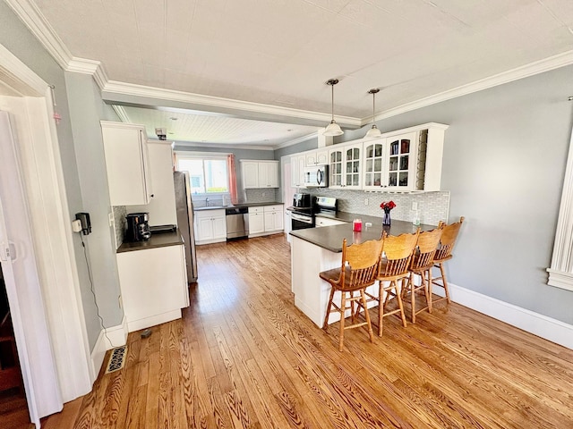 kitchen with appliances with stainless steel finishes, a peninsula, dark countertops, white cabinetry, and light wood finished floors