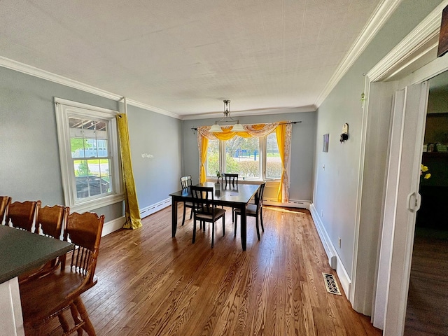 dining space with a baseboard heating unit, plenty of natural light, wood finished floors, ornamental molding, and baseboards