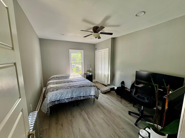 bedroom featuring wood finished floors, a closet, ceiling fan, baseboards, and a desk