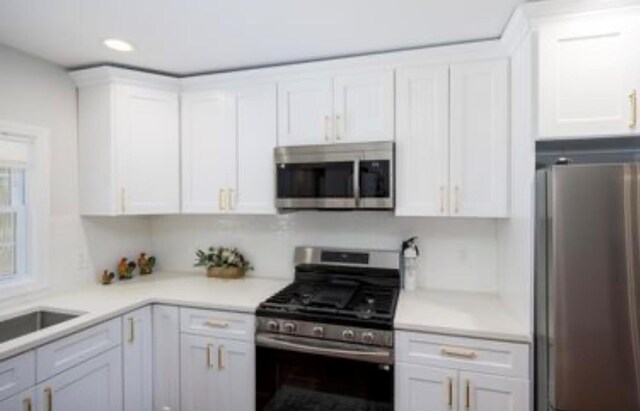 kitchen with appliances with stainless steel finishes, white cabinetry, light countertops, recessed lighting, and a sink
