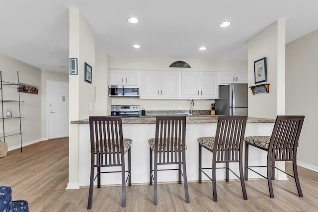259 Dune Rd Unit 128, Westhampton Beach, NY 11978 - kitchen featuring stainless steel appliances, a breakfast bar, white cabinetry, and recessed lighting