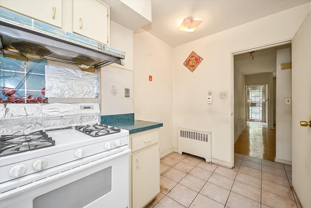148-35 58th Ave, Flushing, NY 11355 - kitchen featuring gas range gas stove, radiator heating unit, under cabinet range hood, light tile patterned floors, and baseboards