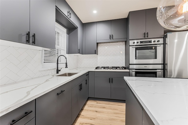 kitchen with a sink, stainless steel appliances, gray cabinets, decorative backsplash, and light wood-style flooring