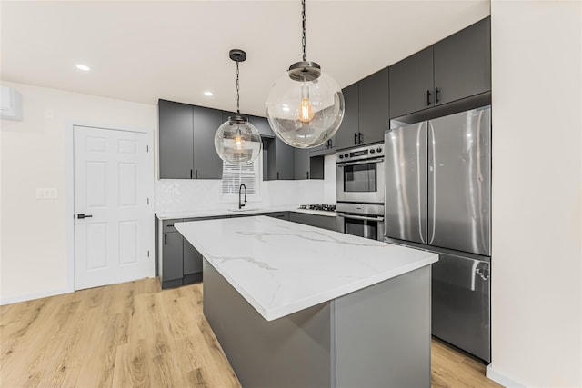 kitchen with appliances with stainless steel finishes, light wood-style floors, a center island, pendant lighting, and tasteful backsplash