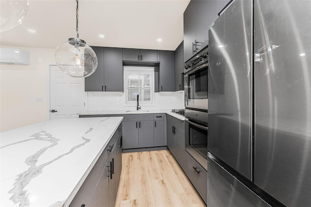 kitchen with stainless steel appliances, gray cabinetry, a sink, light wood finished floors, and tasteful backsplash