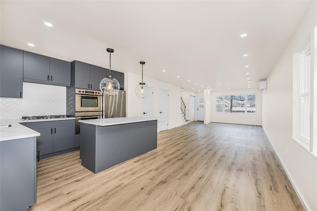 kitchen with appliances with stainless steel finishes, light wood-style flooring, tasteful backsplash, a center island, and light countertops