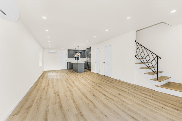 unfurnished living room featuring light wood-style floors, recessed lighting, a wall mounted air conditioner, stairs, and baseboards
