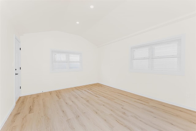 empty room featuring light wood finished floors, vaulted ceiling, and baseboards