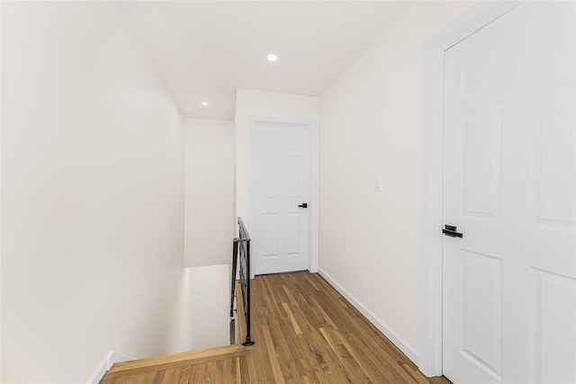 hallway featuring baseboards, wood finished floors, recessed lighting, and an upstairs landing