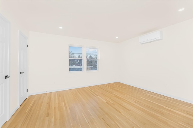 unfurnished room with an AC wall unit, light wood-type flooring, baseboards, and recessed lighting