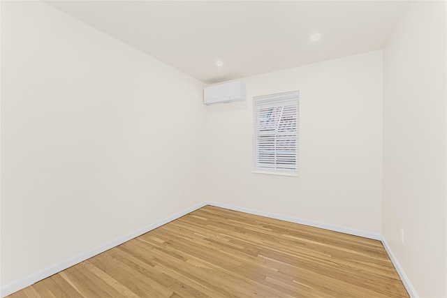unfurnished room with light wood-style flooring, an AC wall unit, and baseboards