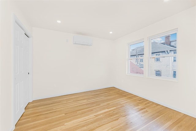 unfurnished bedroom featuring light wood finished floors, baseboards, a wall unit AC, a closet, and recessed lighting