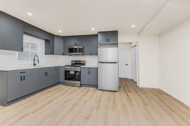 kitchen with stainless steel appliances, a sink, light countertops, gray cabinets, and backsplash
