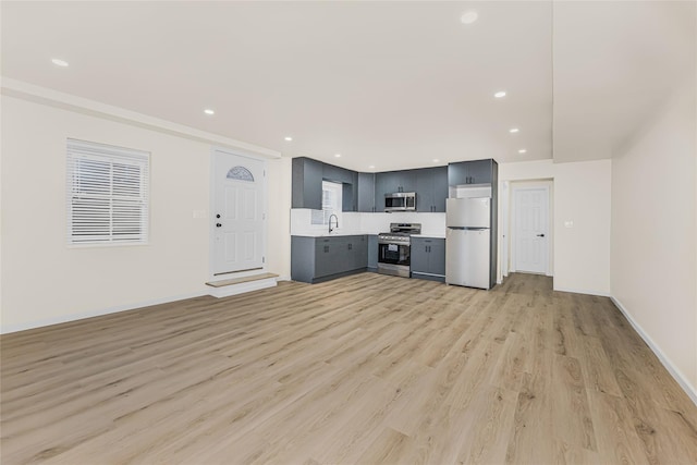 unfurnished living room featuring light wood finished floors, a sink, recessed lighting, and baseboards