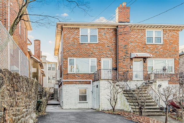 back of house featuring stairs, a chimney, and brick siding