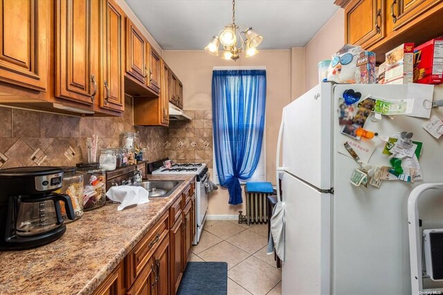 kitchen with white appliances, brown cabinets, a sink, light tile patterned floors, and backsplash