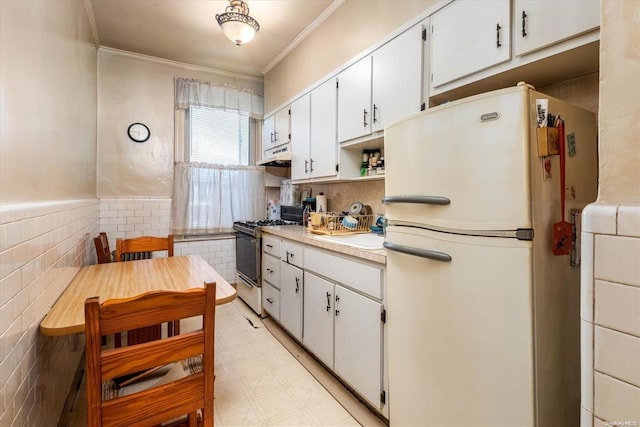 kitchen with freestanding refrigerator, range with gas stovetop, under cabinet range hood, ornamental molding, and light countertops