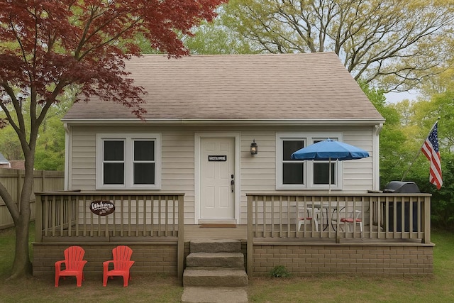 view of front of house with a deck, a shingled roof, and fence