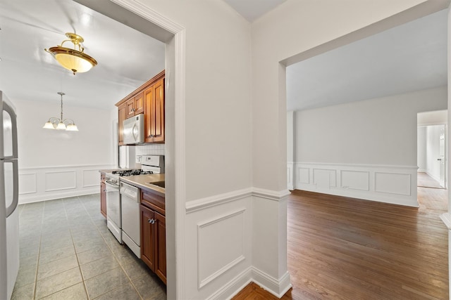kitchen with white appliances, a decorative wall, wainscoting, a chandelier, and hanging light fixtures