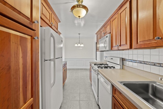 kitchen featuring white appliances, a sink, brown cabinets, a decorative wall, and a wainscoted wall