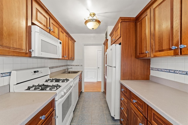 kitchen with white appliances, a sink, brown cabinetry, tasteful backsplash, and light countertops