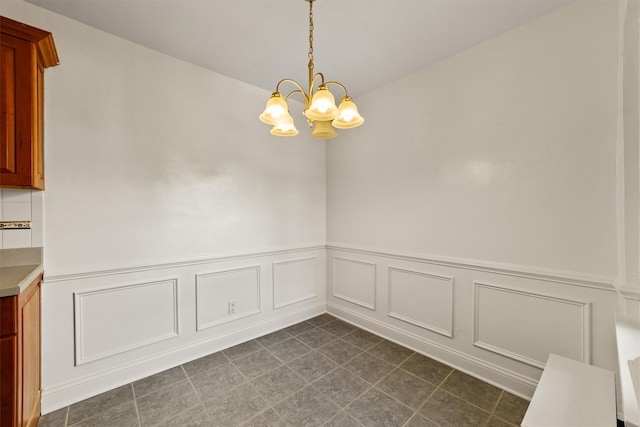 unfurnished dining area with a chandelier, wainscoting, and a decorative wall