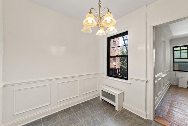 unfurnished dining area with a chandelier, plenty of natural light, a wainscoted wall, a decorative wall, and dark tile patterned floors